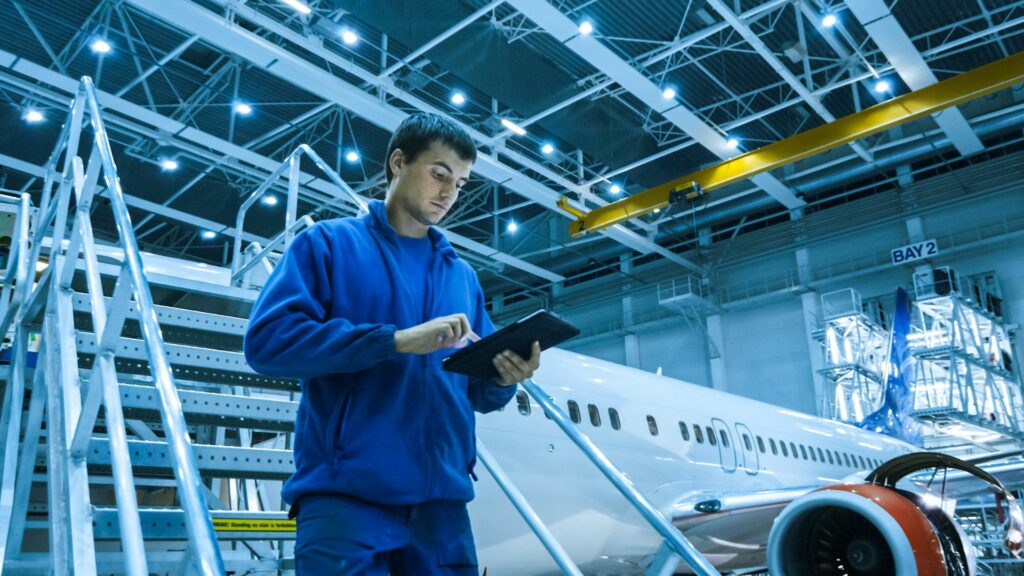 A man is standing looking at an Ipad infront of an airplane