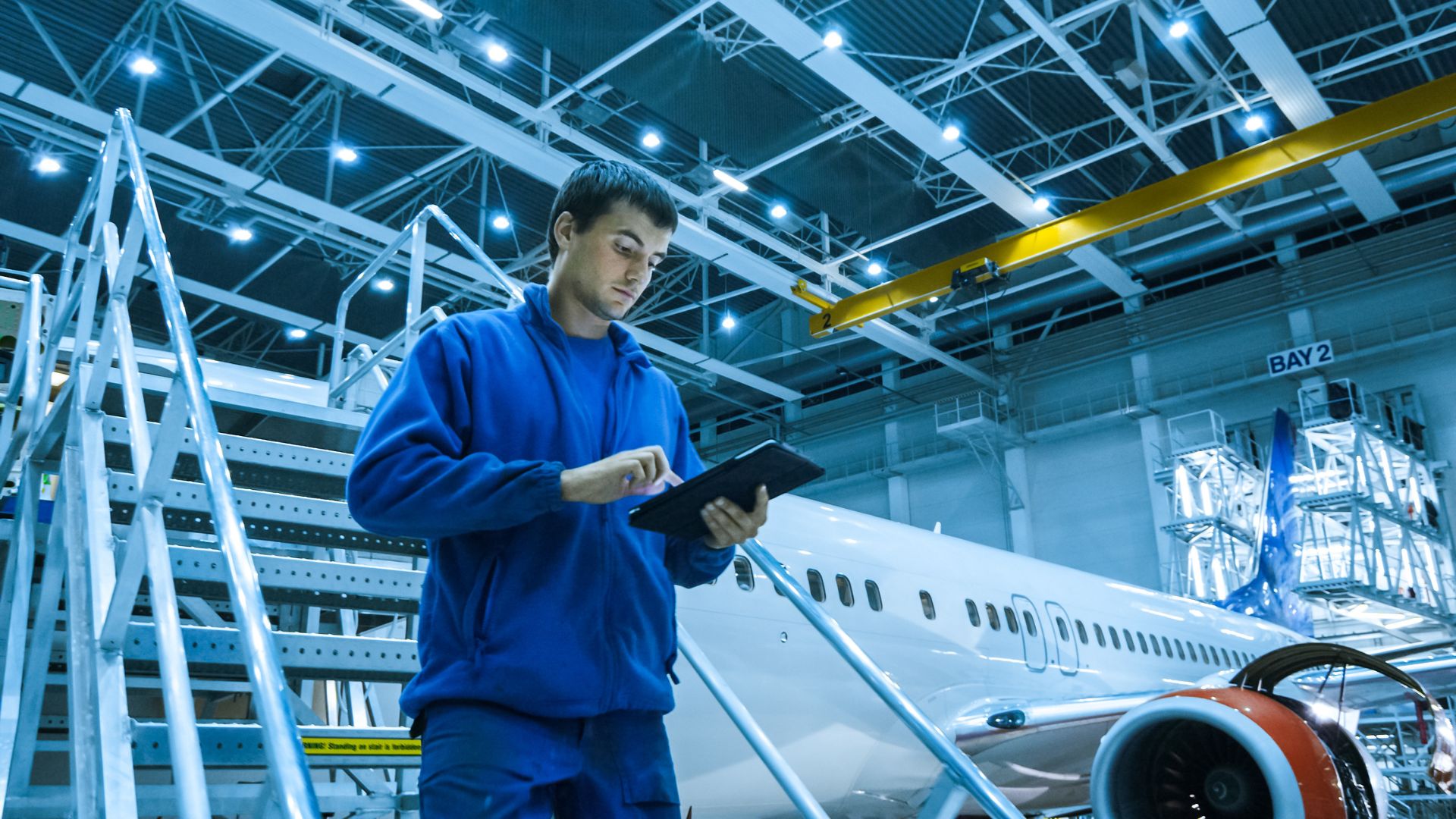 A man is standing looking at an Ipad infront of an airplane
